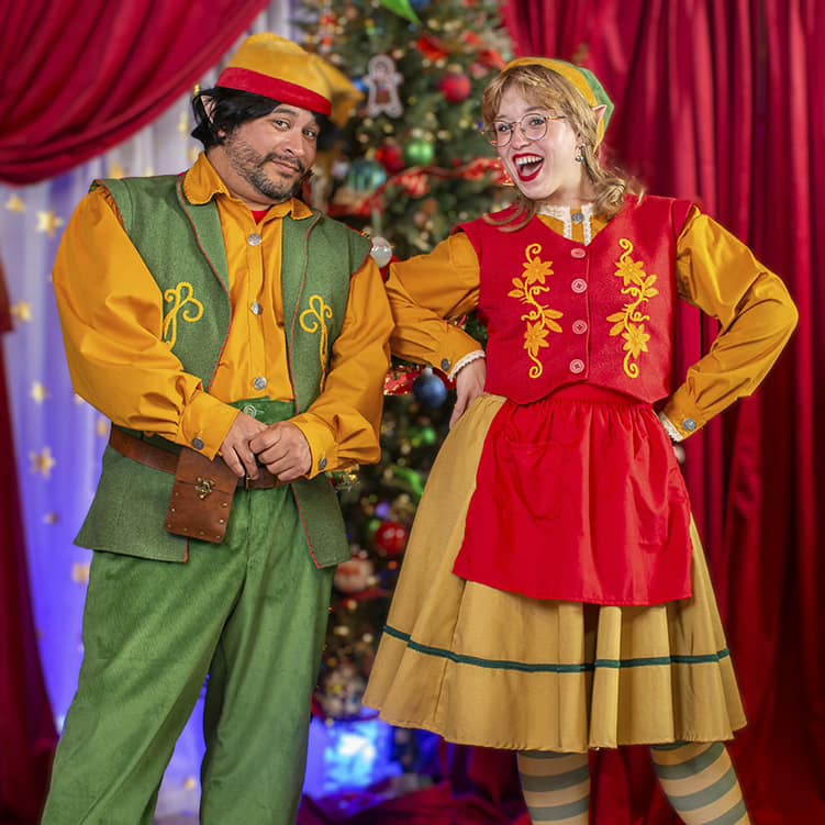 Two playful House of Kringle elves posing in front of a Christmas tree.