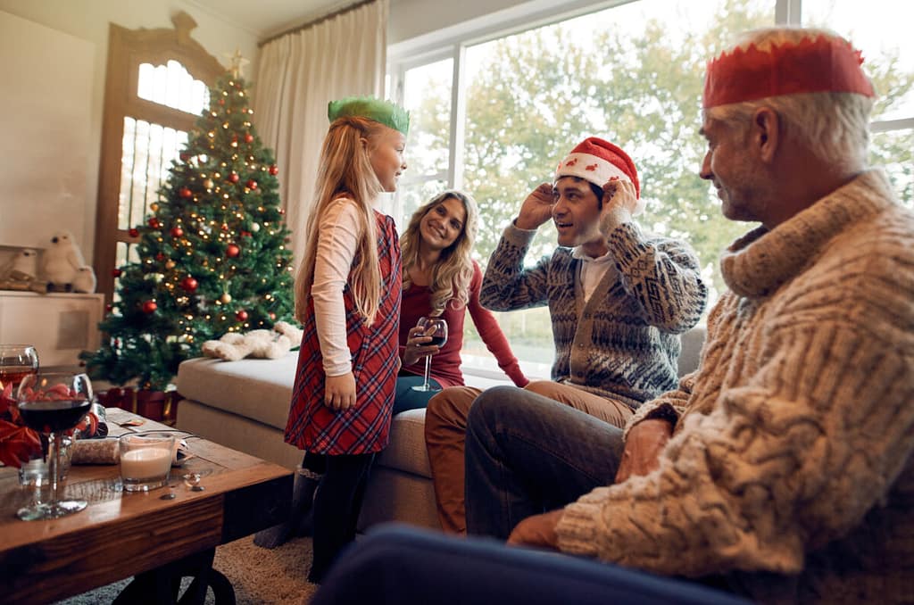 Happy family at home wearing santa hat and christmas crown on christmas eve. Little girl with her parents and grandparents celebrating christmas.