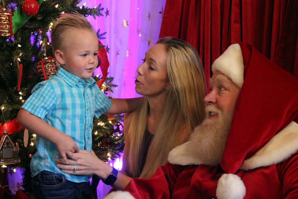 photo of a young mother introducing her toddler son to santa claus beside a christmas tree