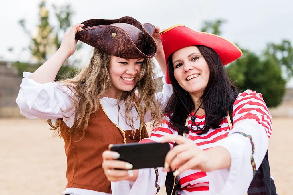 Two Young Happy Smiling Caucasian Women In Pirate Costumes Taking Selfie On Smartphone