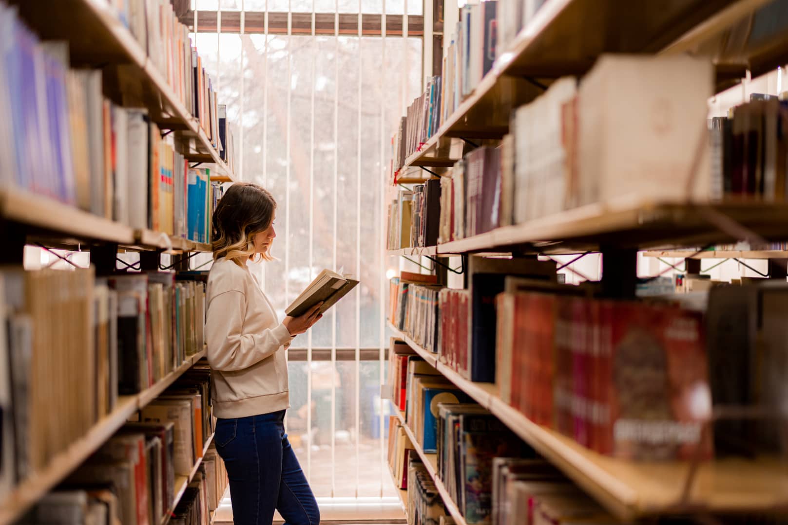 A person reading a book in a library with shelves of books in the background