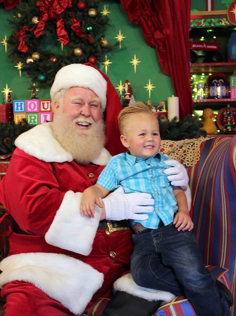 Photo of Santa Claus and a toddler posing for a picture in the House of Kringle